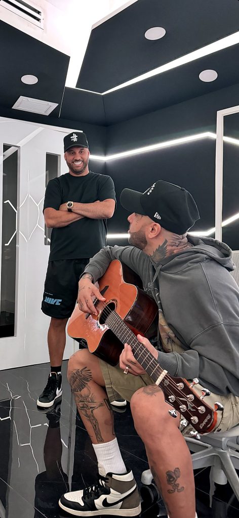 Nicky Jam y Valentino en un estudio de paredes negras y líneas blancas.
